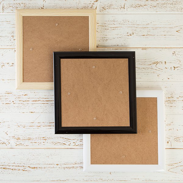 Three plastic Craft Buddy Greetings Cards Frames laid diagonally, one each of wood-effect, black and white finishes

