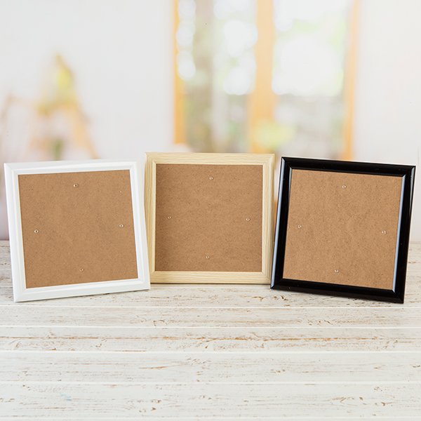 lifestyle image of three Crystal Art Greetings Card Frames on table in front of a window. Pictured are one each of white, wood-effect and black finish.